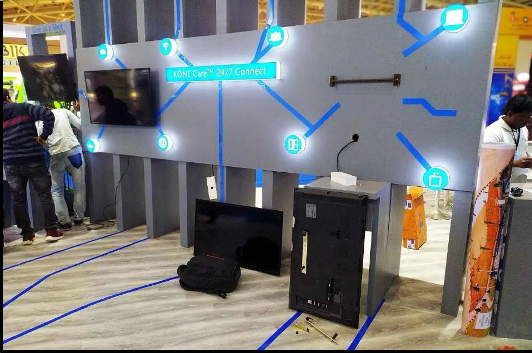 A KONE exhibition wall part-way through install, the graphic panel mounted and lit while cabling and a toolkit still sit on the floor
