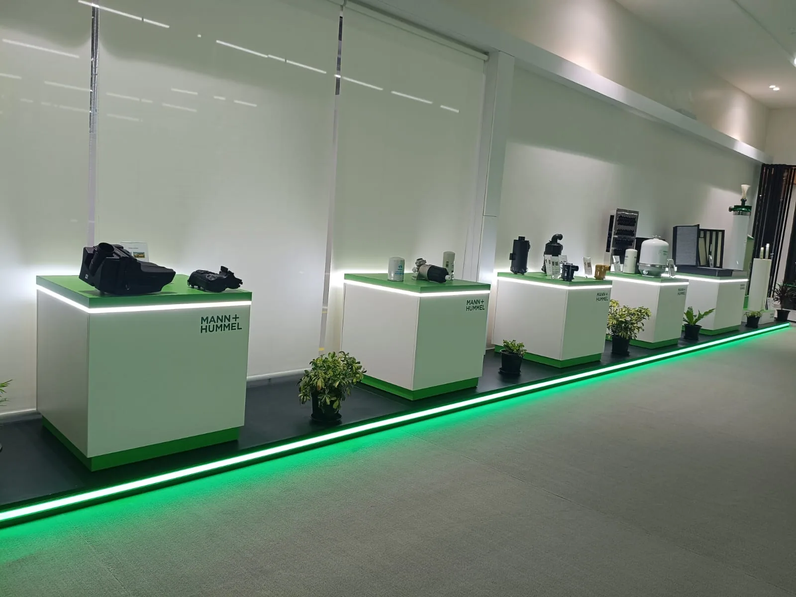 A line of white product plinths with green tops receding along a continuous green LED floor line inside a brand experience centre