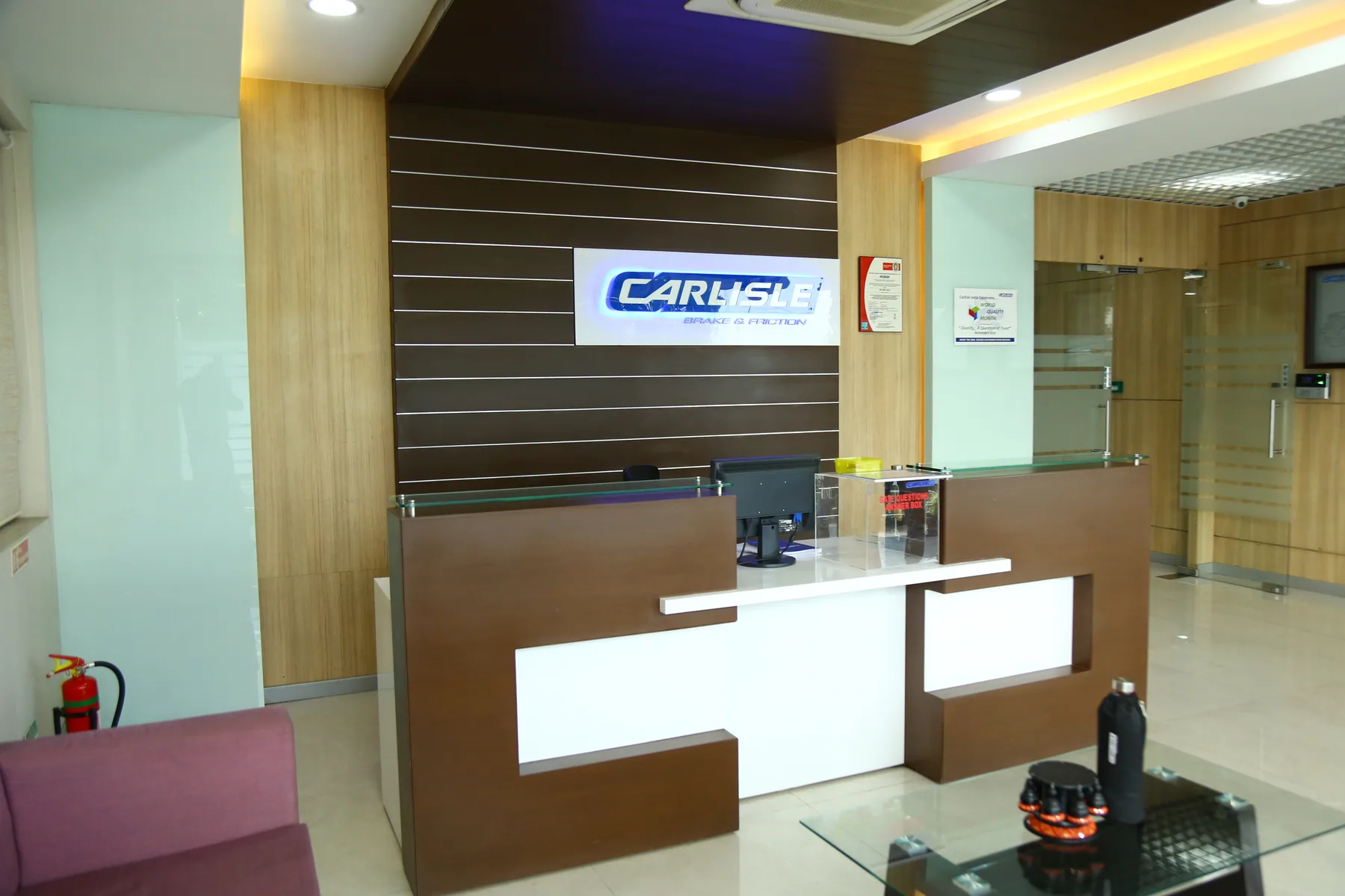 A technical workplace reception desk in timber and glass beneath an illuminated ceiling detail